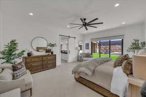 Bedroom with a barn door, ensuite bath, access to exterior, a ceiling fan, and carpet flooring