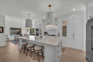Kitchen with white cabinets, parquet flooring, a kitchen bar, and light stone counters