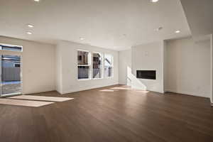 Unfurnished living room featuring dark wood-style floors, a glass covered fireplace, a textured ceiling, and recessed lighting