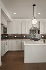 Kitchen with white cabinetry, light stone counters, decorative light fixtures, dark wood-style floors, and decorative backsplash