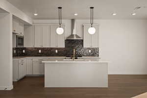 Kitchen featuring dark wood finished floors, hanging light fixtures, an island with sink, and white cabinetry