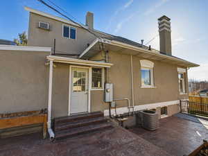 Back of house featuring a chimney, stucco siding, and entry steps