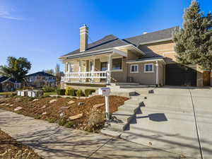 View of front facade with a chimney, a porch, stucco siding, driveway, and roof with shingles