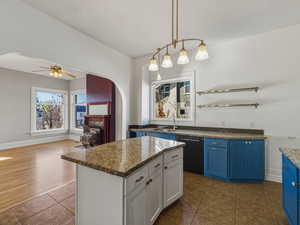 Kitchen with arched walkways, hanging light fixtures, a kitchen island, ceiling fan, and dark stone counters