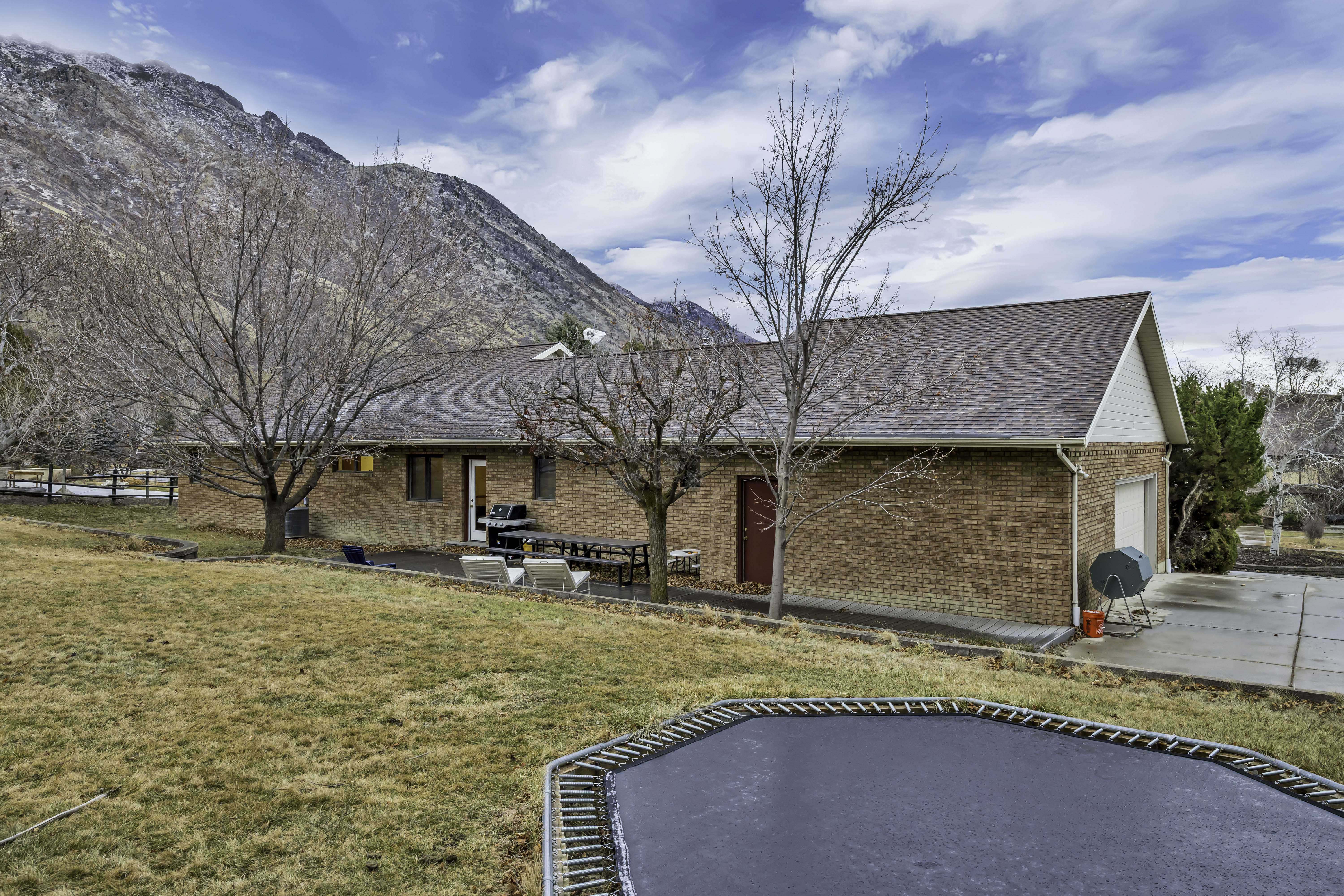 Back of house featuring a trampoline, a patio area, a yard, a mountain view, and brick siding