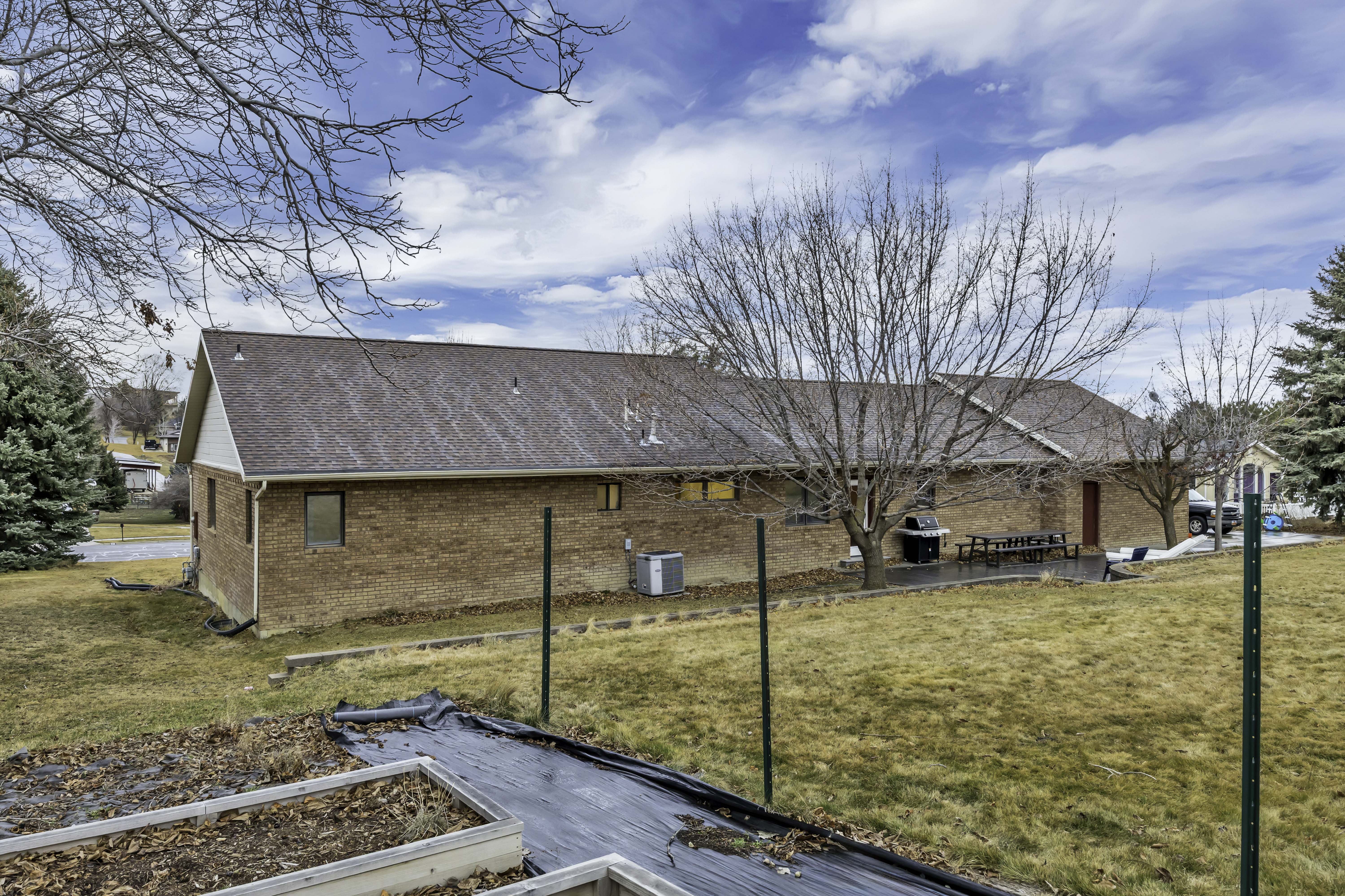 View of side of property featuring brick siding, a shingled roof, a yard, a patio, and a vegetable garden