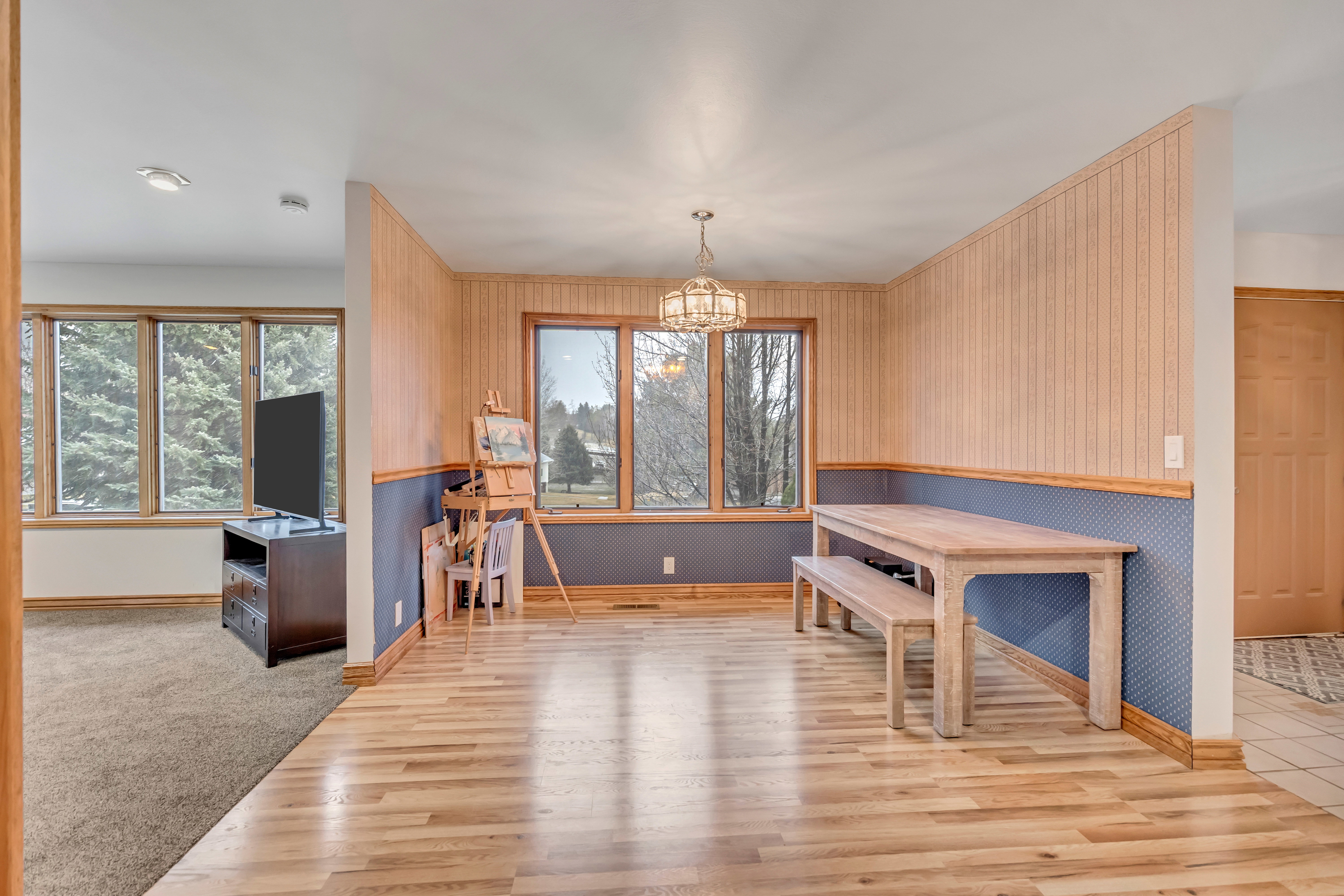 Dining area with wallpapered walls, light wood-style floors, wainscoting, a chandelier, and healthy amount of natural light
