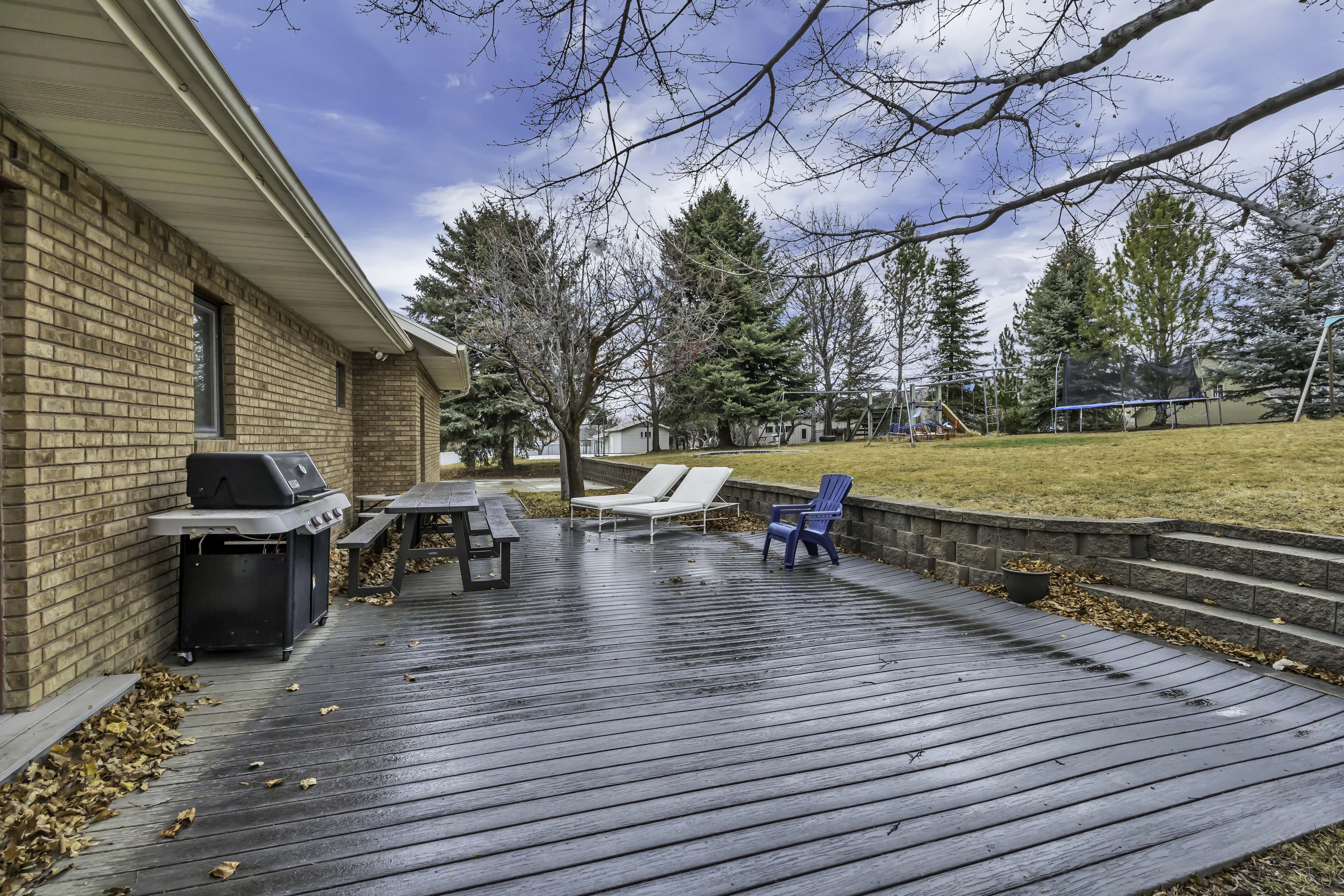 Wooden deck with a trampoline, a playground, grilling area, and a lawn