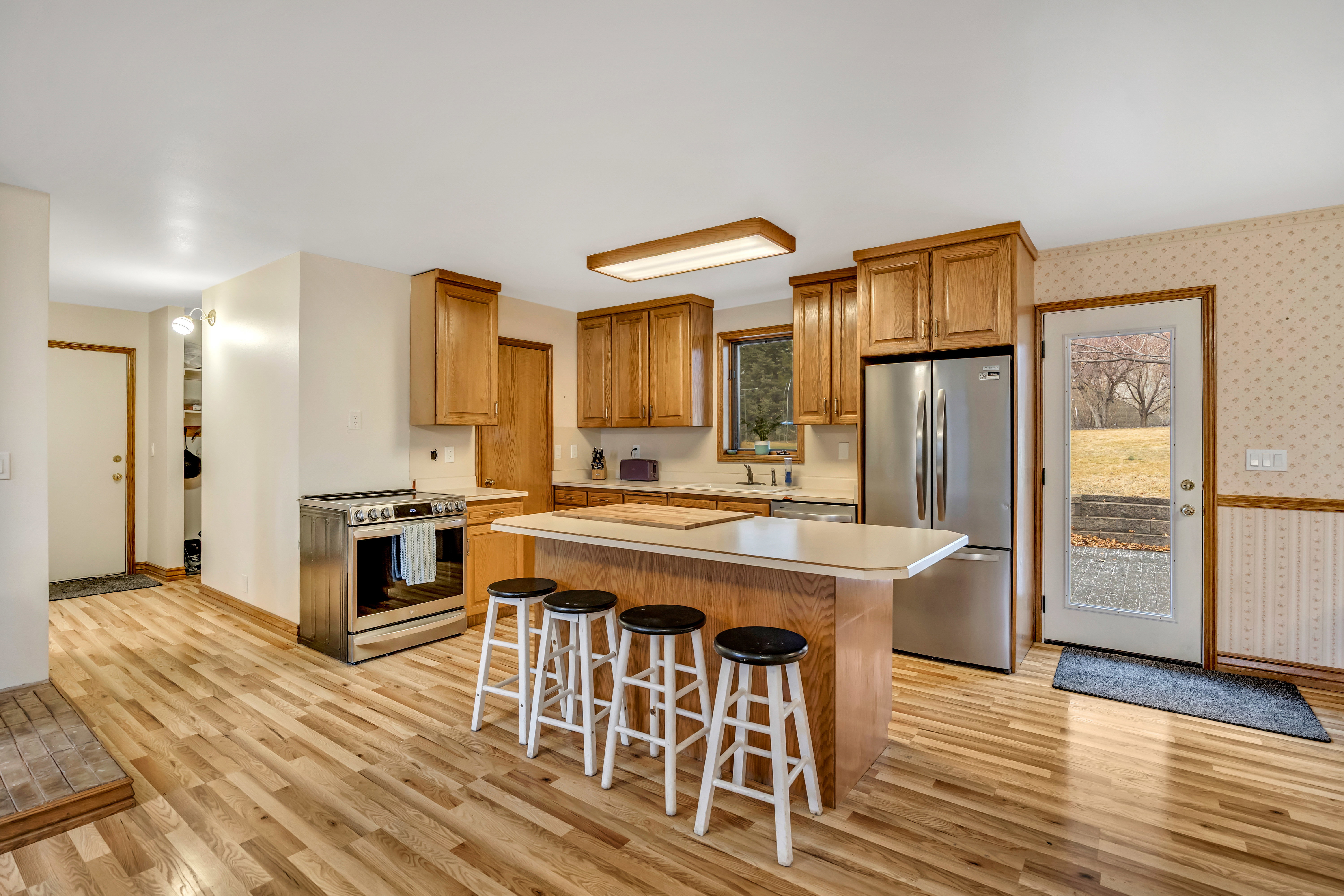 Kitchen featuring light countertops, stainless steel appliances, wallpapered walls, a kitchen breakfast bar, and a center island