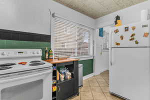 Kitchen featuring white appliances, light tile patterned floors, a wainscoted wall, wooden counters, and electric panel