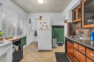 Kitchen featuring white appliances, glass insert cabinets, wood finish cabinetry, a wainscoted wall, and dark countertops