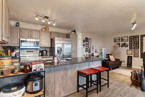 Kitchen featuring a breakfast bar, stainless steel appliances, backsplash, dark stone countertops, and light wood-type flooring