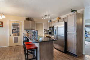 Kitchen with a breakfast bar area, stainless steel appliances, dark stone counters, tasteful backsplash, and dark wood-type flooring