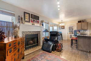 Living room with light wood-style floors, a textured ceiling, hanging lights, and a fireplace