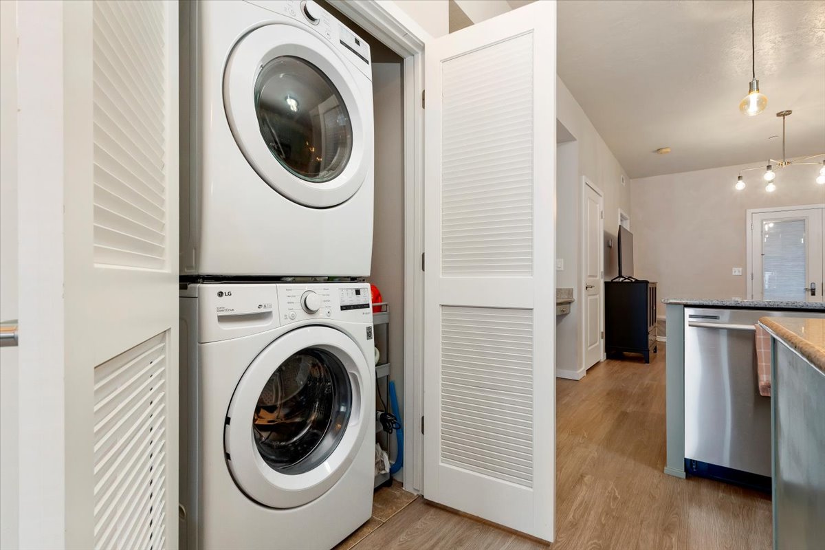 Laundry area with stacked washer / drying machine and light wood finished floors