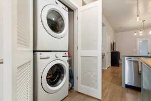 Laundry area with stacked washer / drying machine and light wood finished floors