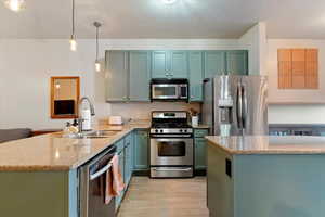 Kitchen featuring stainless steel appliances, light stone countertops, a peninsula, pendant lighting, and green cabinets