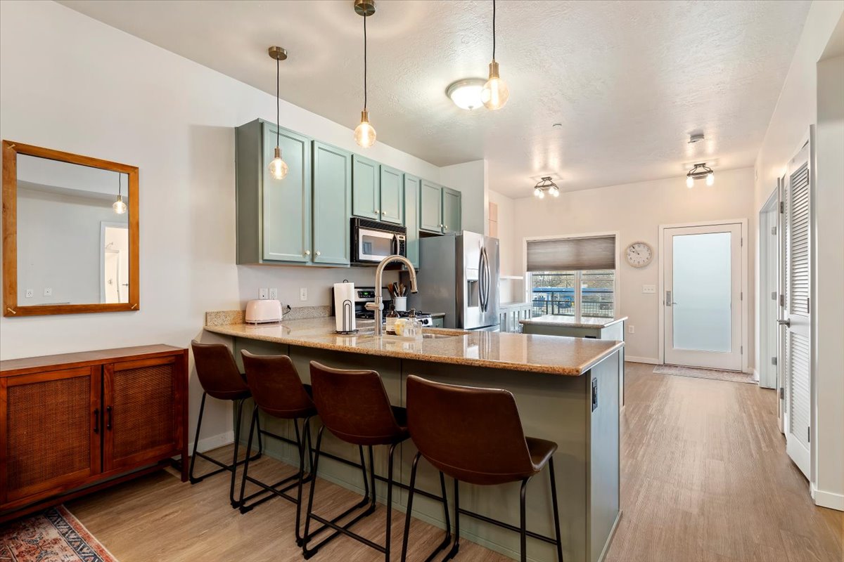 Kitchen with light stone counters, green cabinets, a peninsula, and light wood-type flooring