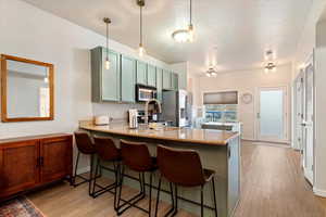 Kitchen with light stone counters, green cabinets, a peninsula, and light wood-type flooring