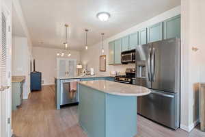 Kitchen with stainless steel appliances, decorative light fixtures, light stone counters, light wood-type flooring, and a peninsula