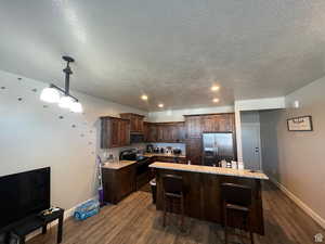 Kitchen with dark wood finish cabinetry, stainless steel appliances, pendant lighting, dark wood-style floors, and a textured ceiling