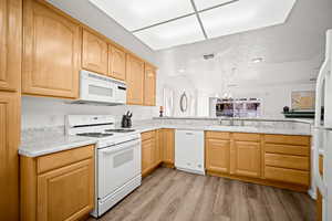 Kitchen with white appliances, light wood-style floors, light wood finish cabinetry, and light countertops