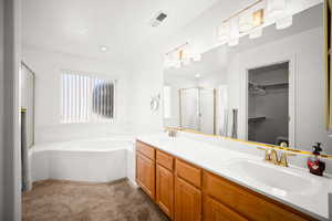 Full bathroom with a walk in closet, double vanity, dark carpet, a garden tub, and a shower stall