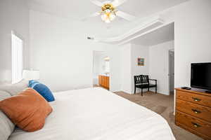 Bedroom with light colored carpet, ceiling fan, and connected bathroom