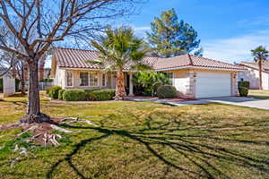 View of front of property with a front yard, an attached garage, stucco siding, and a tile roof