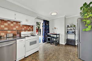 Kitchen with stainless steel appliances, backsplash, white cabinetry, ornamental molding, and dark countertops