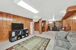 Carpeted living room with a wood stove, wood walls, and a heating unit