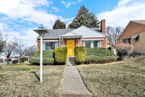 View of front of house featuring brick siding, a front yard, a chimney, and roof with shingles