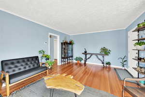Living area with hardwood / wood-style floors, a textured ceiling, and crown molding
