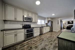 Kitchen featuring stainless steel appliances, cream cabinetry, dark wood-style flooring, tasteful backsplash, and recessed lighting