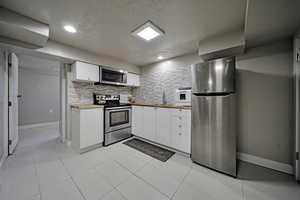 Kitchen featuring white cabinets, stainless steel appliances, tasteful backsplash, light tile patterned floors, and a textured ceiling