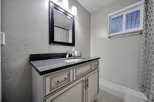 Bathroom with vanity, curtained shower, light tile patterned flooring, and a textured wall