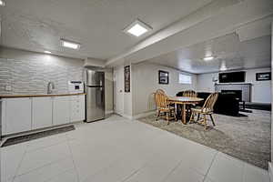 Kitchen featuring white cabinets, a textured ceiling, a fireplace, freestanding refrigerator, and decorative backsplash