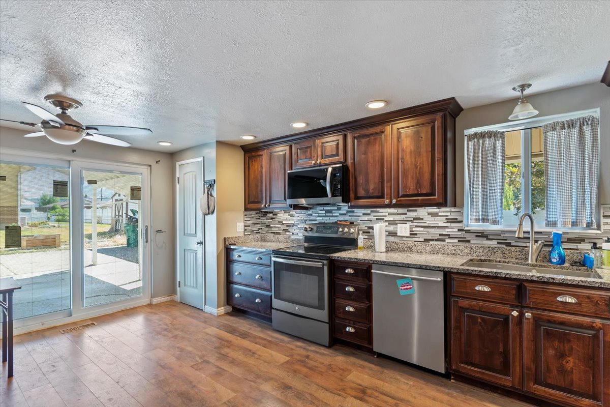 Kitchen featuring stainless steel appliances, dark wood finish cabinets, ceiling fan, dark wood finished floors, and light stone counters