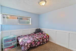 Carpeted bedroom featuring a decorative wall, a wainscoted wall, and a textured ceiling