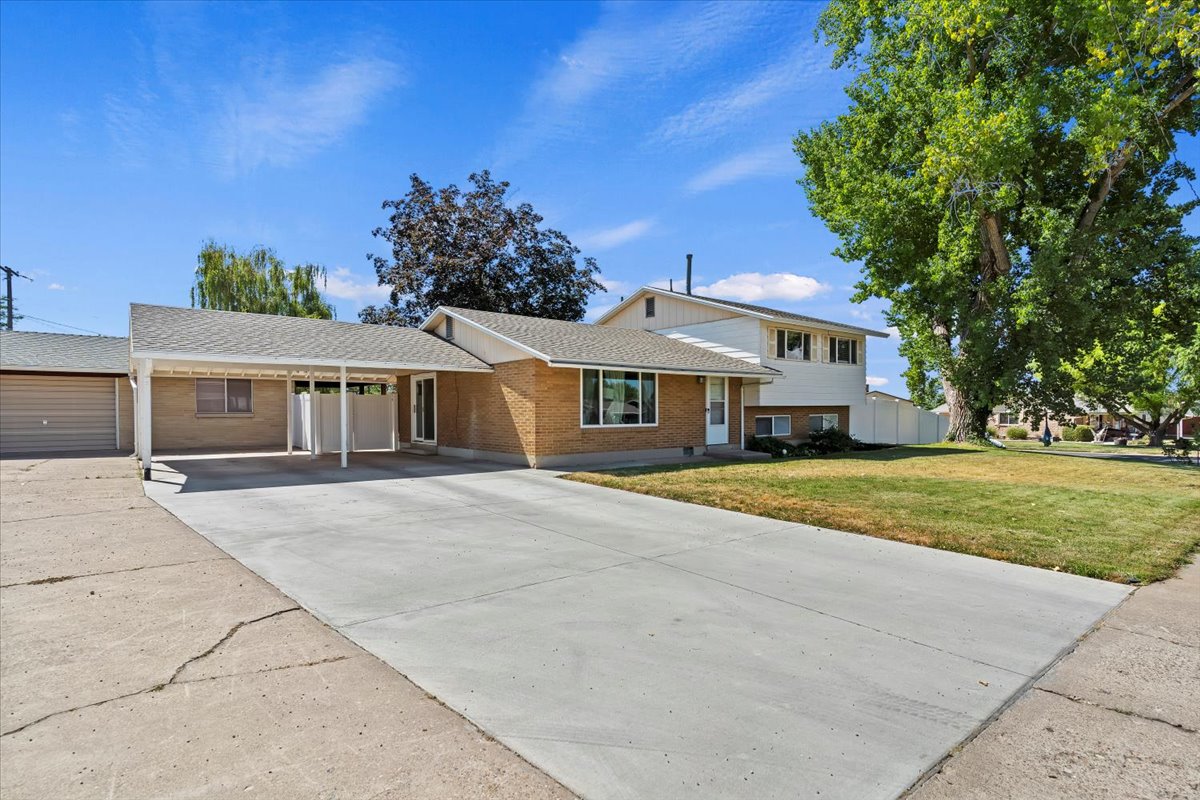 Split level home with a carport, brick siding, a front lawn, driveway, and a shingled roof