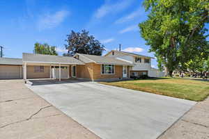 Split level home with a carport, brick siding, a front lawn, driveway, and a shingled roof
