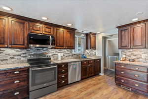 Kitchen with stainless steel appliances, light wood-type flooring, light stone counters, dark wood finish cabinets, and a textured ceiling