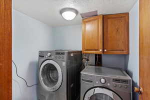 Laundry area with cabinet space, a textured ceiling, and separate washer and dryer