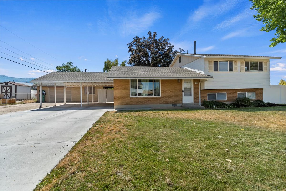 Split level home with brick siding, concrete driveway, a front lawn, and a carport