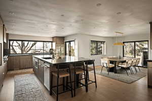 Kitchen with a kitchen island with sink, modern cabinets, light wood finished floors, a kitchen breakfast bar, and decorative light fixtures
