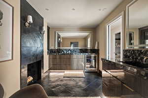 Full bathroom with double vanity, wine cooler, stone tile floors, and a tile fireplace