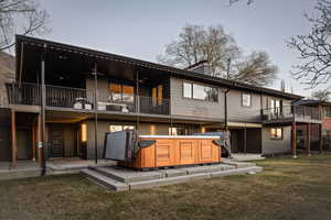 Back of house featuring a hot tub, brick siding, a chimney, a yard, and a patio area