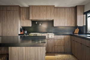 Kitchen with dark stone counters, modern cabinets, light wood finished floors, decorative backsplash, and wood finish cabinetry