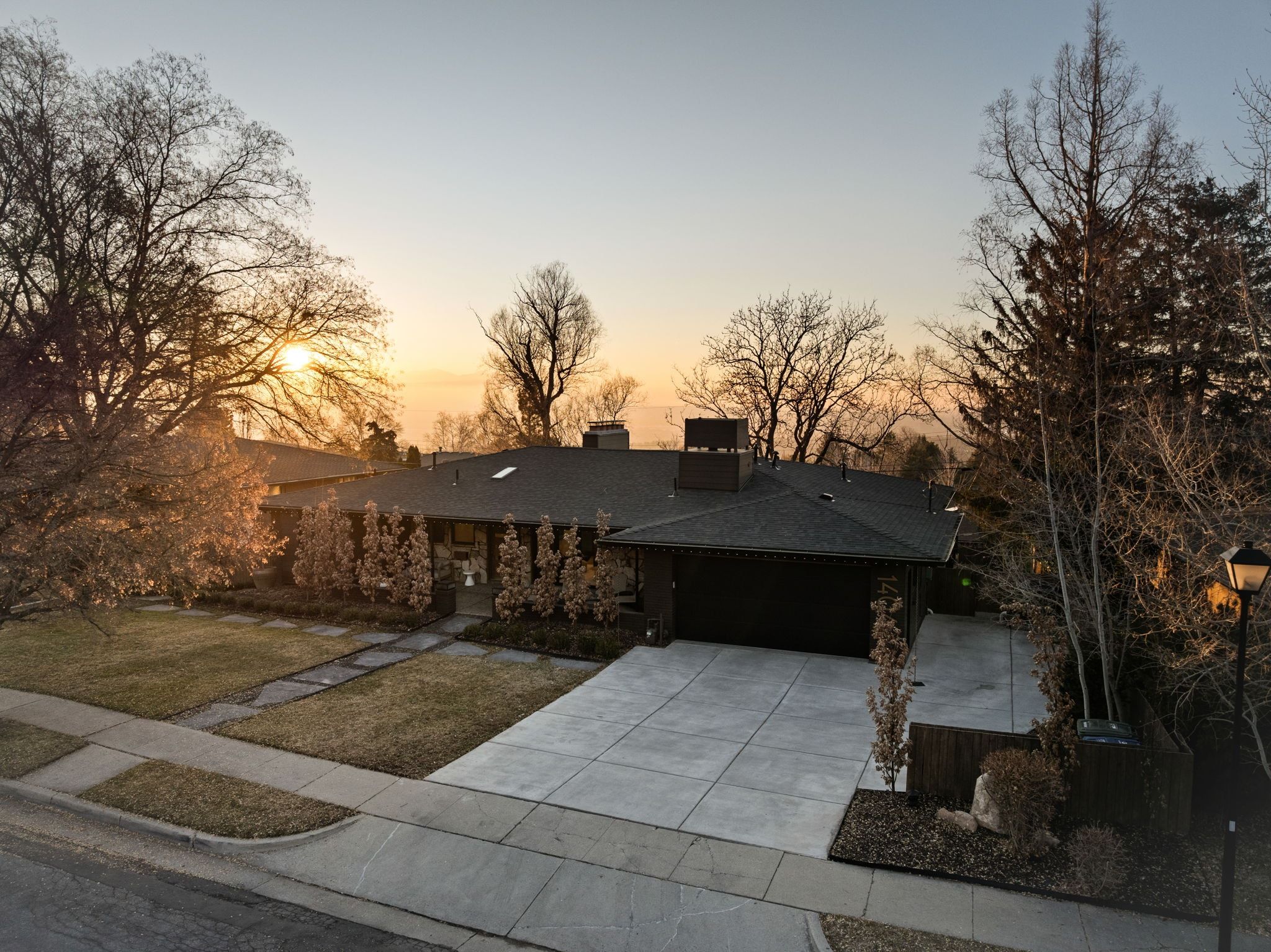 Mid-century inspired home with concrete driveway, a garage, a front yard, a chimney, and a shingled roof