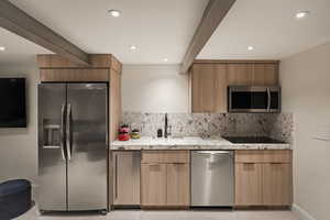 Kitchen featuring stainless steel appliances, light stone counters, backsplash, modern cabinets, and beam ceiling